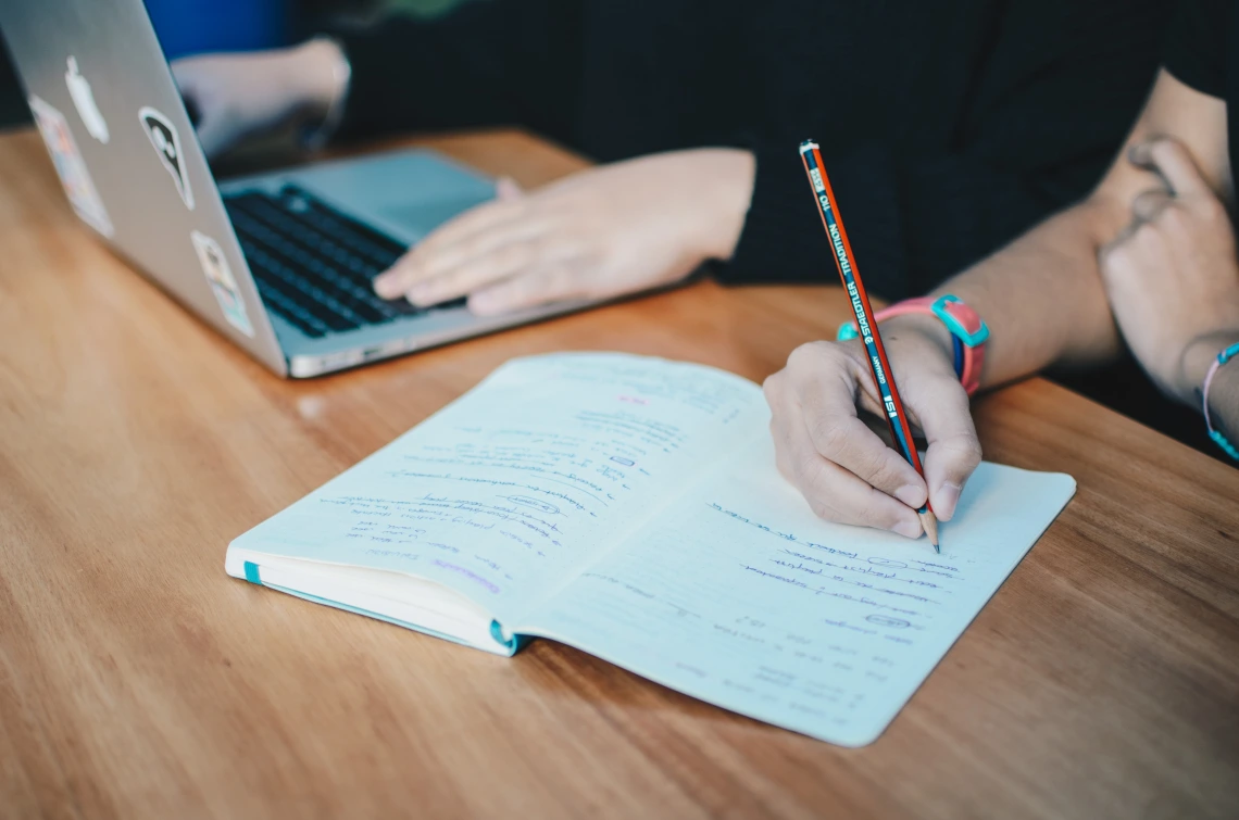 person on laptop and person taking notes in notepad