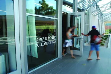 Students walk out the glass doors of the University of Arizona Law building